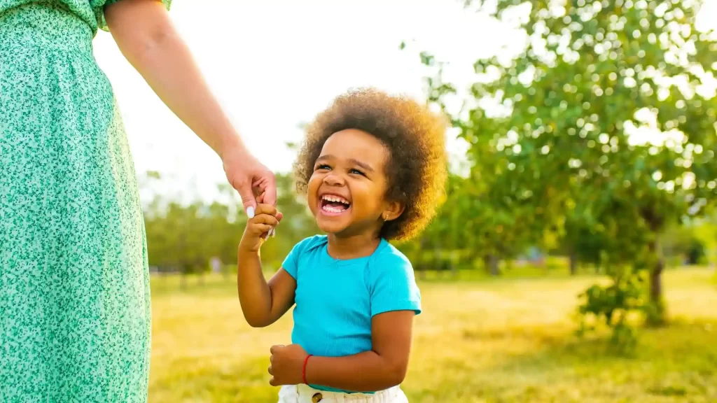 a child laughing and holding a hand of a legal guardian