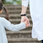 Close-up of an adult and child holding hands while walking up outdoor steps.