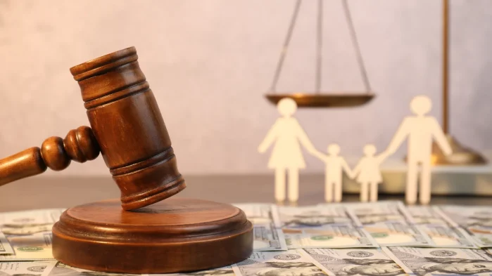 Gavel, scale of justice, and family cut-out figures with money on the table symbolizing family law and finances.