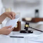Person opening an envelope with a gavel and legal documents on the table.